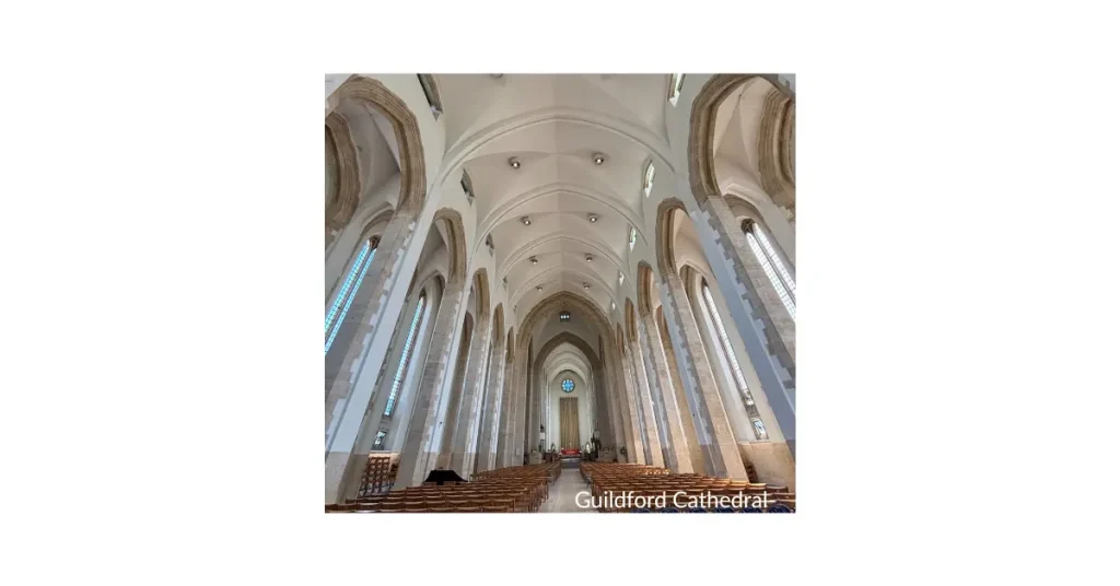 Interior view of Guildford Cathedral, showing the high vaulted ceiling, nave, and tall, narrow windows in a modern Gothic style.