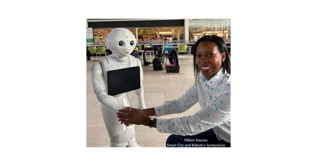 Beverly Clarke MBE interacting with a white humanoid Pepper robot holding a tablet at the Milton Keynes Smart City and Robotics Symposium.