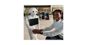 Beverly Clarke MBE interacting with a white humanoid Pepper robot holding a tablet at the Milton Keynes Smart City and Robotics Symposium.